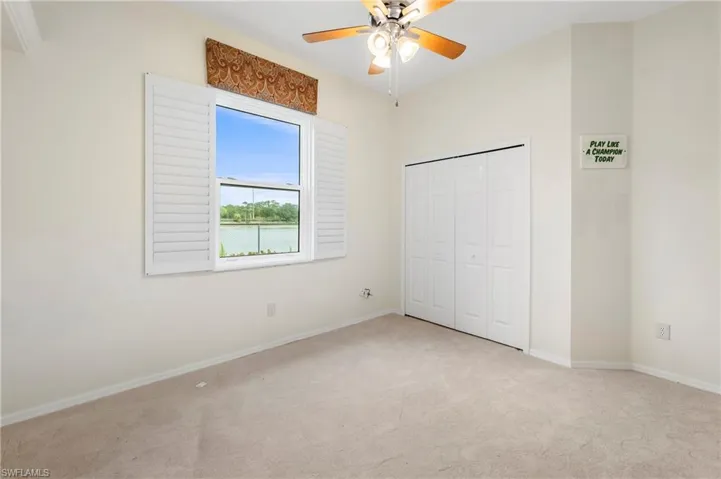 Carpeted room with a ceiling fan, a window with plantation shutters, and a water view