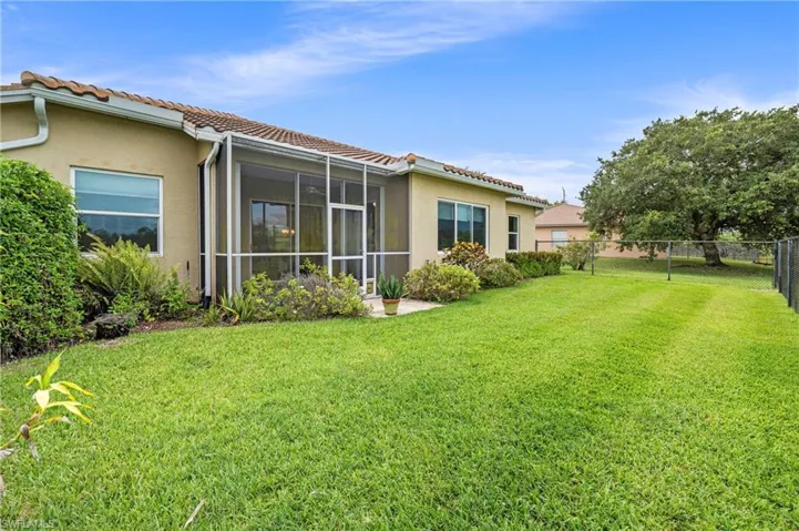 Expansive backyard featuring a screened patio, mature landscaping, and a chain-link fence