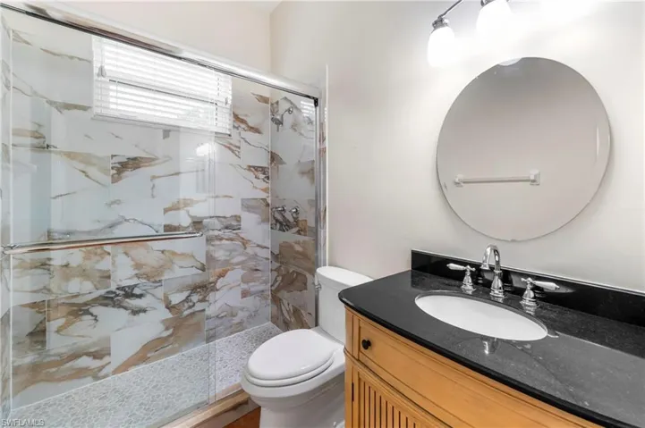 Bathroom featuring a shower with glass sliding doors, marble-patterned tile, and a pebble-style shower floor