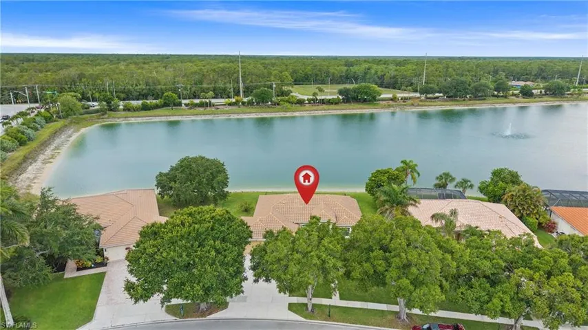 Lakefront property featuring a tile roof, mature trees, green landscaping, and a paved driveway