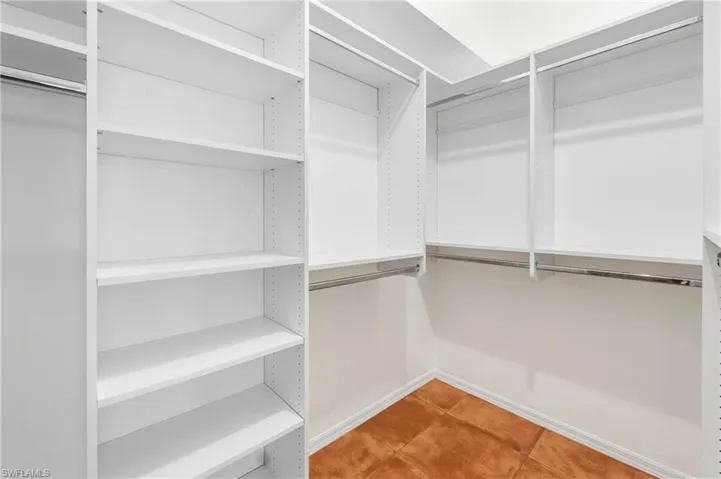 Walk-in closet featuring white shelving units, multiple hanging rods, and terra cotta floor tiles