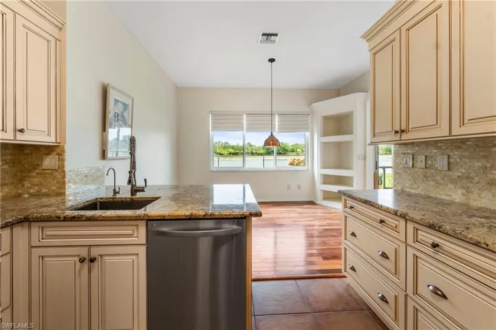 Kitchen featuring stone countertops, tile backsplash, stainless steel dishwasher, and cream-colored cabinetry