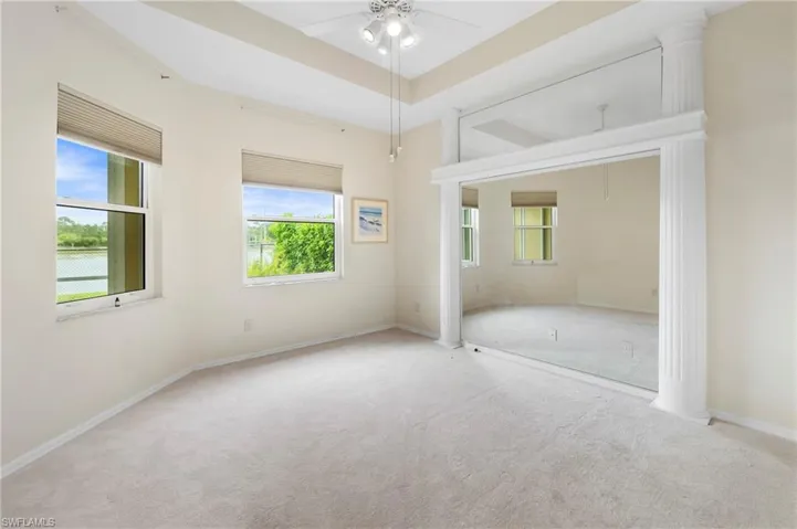 Spacious room featuring light-colored carpeting, two windows with horizontal blinds, a tray ceiling, and a ceiling fan with integrated lighting