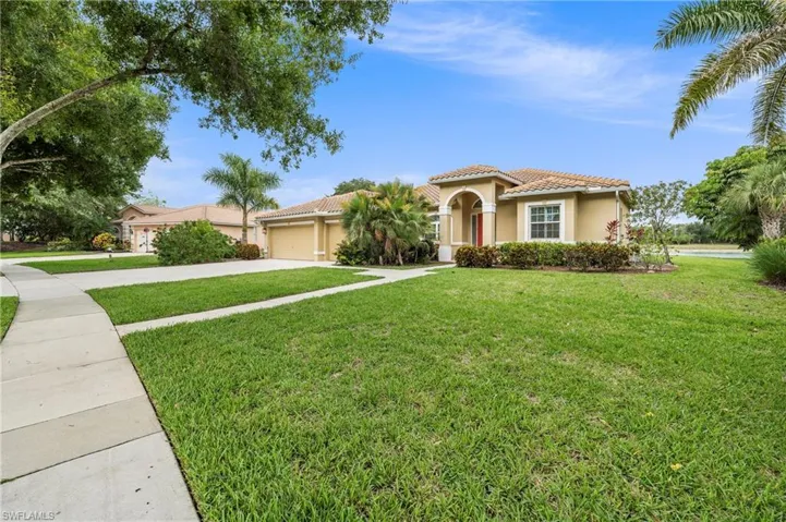 Mediterranean-style exterior featuring a tile roof, arched entry, two-car garage, mature landscaping, and a well-maintained lawn