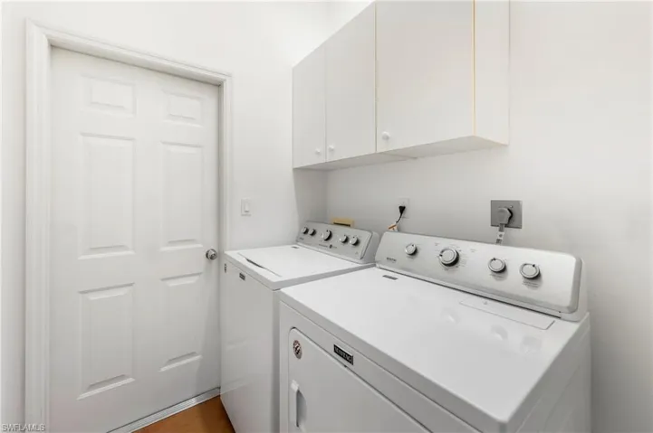 Dedicated laundry area featuring a white six-panel door, built-in white cabinetry, light wood-finish flooring, and white walls