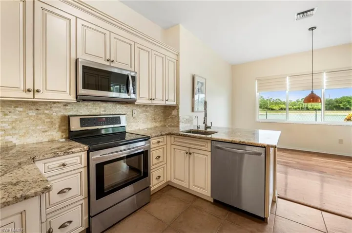 Kitchen featuring cream-colored cabinetry, stainless steel appliances, granite countertops, and a mosaic tile backsplash