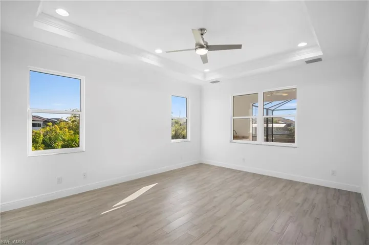 Empty room featuring light wood-style floors, ornamental molding, a ceiling fan, recessed lighting, and a tray ceiling