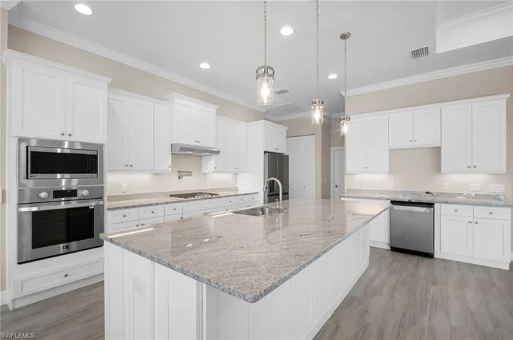 Kitchen featuring stainless steel appliances, white cabinets, pendant lighting, crown molding, and light stone counters