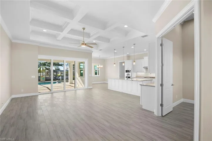 Unfurnished living room featuring ornamental molding, coffered ceiling, beam ceiling, ceiling fan, and light wood finished floors