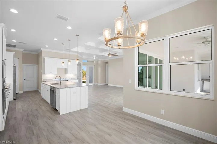 Kitchen featuring crown molding, ceiling fan, white cabinetry, light stone counters, and open floor plan
