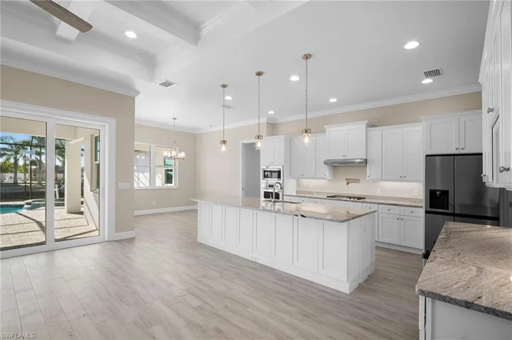 Kitchen with white cabinetry, crown molding, light stone counters, decorative light fixtures, and recessed lighting