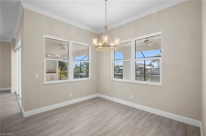 Unfurnished dining area featuring a chandelier, ornamental molding, a ceiling fan, light wood finished floors, and healthy amount of natural light
