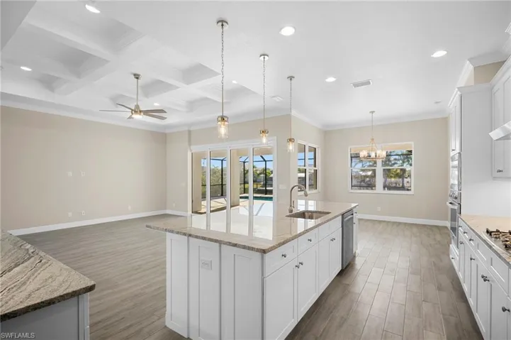 Kitchen with white cabinetry, pendant lighting, coffered ceiling, ornamental molding, and light stone counters