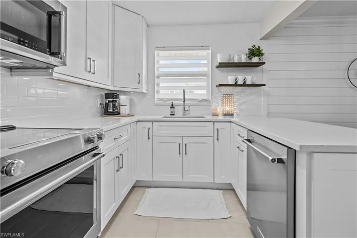 Kitchen featuring appliances with stainless steel finishes, a peninsula, white cabinetry, light stone counters, and tasteful backsplash