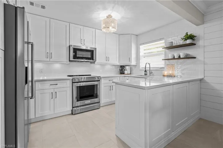 Kitchen with tasteful backsplash, open shelves, appliances with stainless steel finishes, a peninsula, and beam ceiling