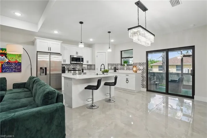 Kitchen featuring stainless steel appliances, decorative backsplash, open floor plan, light countertops, and white cabinets