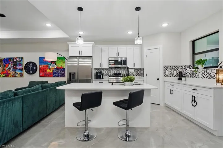Kitchen featuring stainless steel appliances, tasteful backsplash, light countertops, white cabinetry, and a breakfast bar