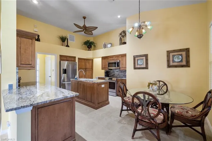 Kitchen featuring hanging light fixtures, appliances with stainless steel finishes, a kitchen island, light stone counters, and kitchen peninsula