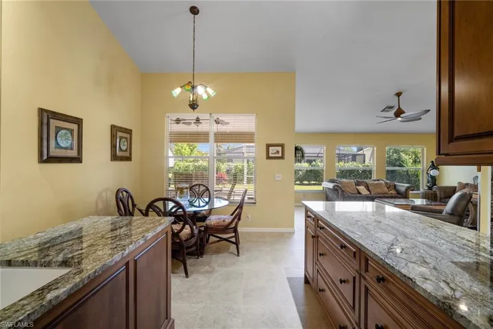 Kitchen with light stone countertops, sink, pendant lighting, light tile patterned flooring, and ceiling fan with notable chandelier