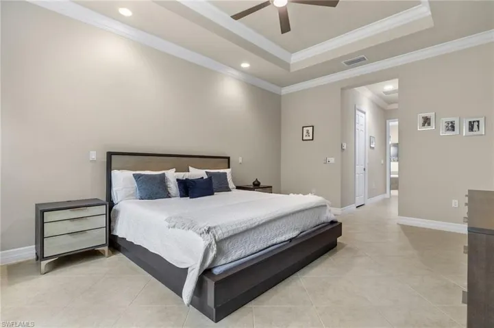 Tiled bedroom with ornamental molding, ceiling fan, and a raised ceiling