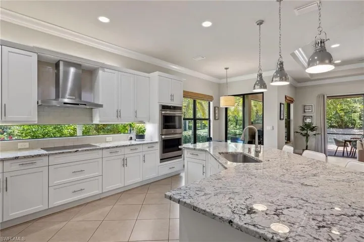 Kitchen featuring wall chimney range hood, stainless steel double oven, backsplash, pendant lighting, and sink