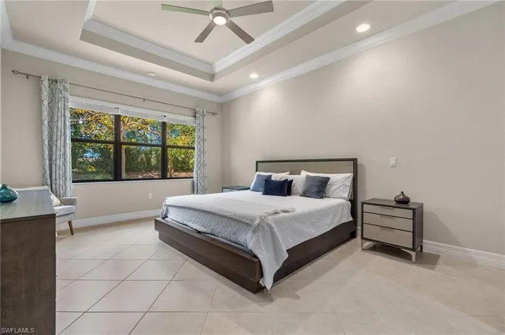 Tiled bedroom featuring ceiling fan, a tray ceiling, and crown molding