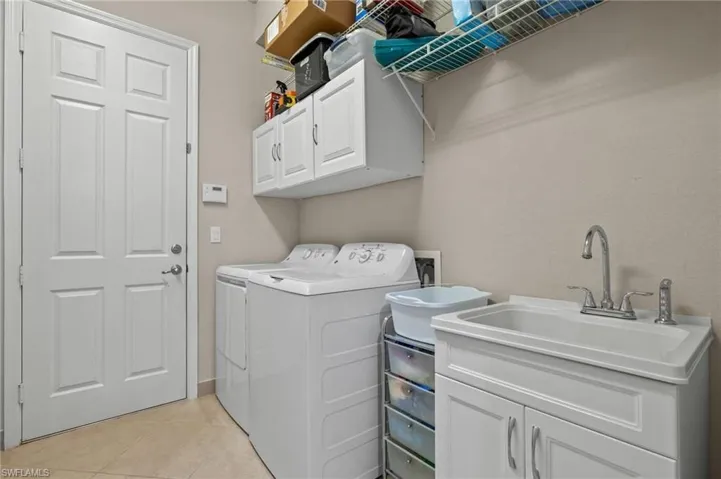 Laundry area with independent washer and dryer, sink, cabinets, and light tile floors