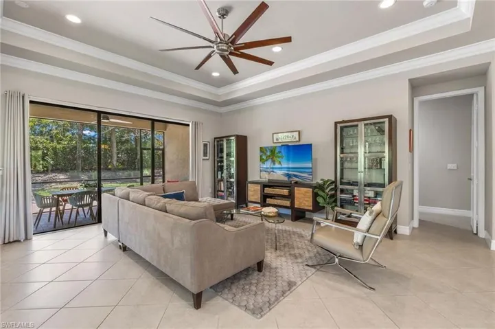 Living room with a tray ceiling, ornamental molding, ceiling fan, and light tile floors