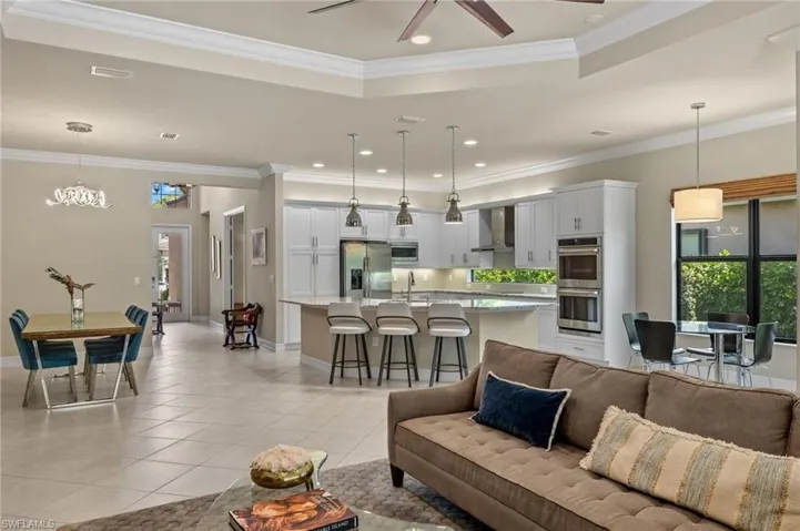 Tiled living room with ceiling fan with notable chandelier, a tray ceiling, crown molding, and sink