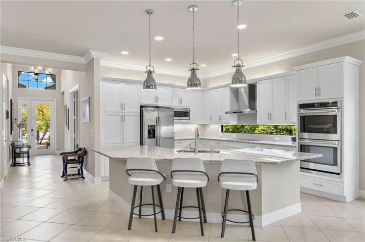 Kitchen featuring wall chimney range hood, stainless steel appliances, a center island with sink, and hanging light fixtures