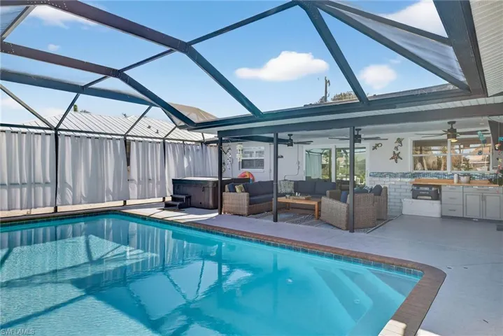 Swimming pool with glass enclosure, a hot tub, an outdoor kitchen and area to lounge, a sunroom, and a patio