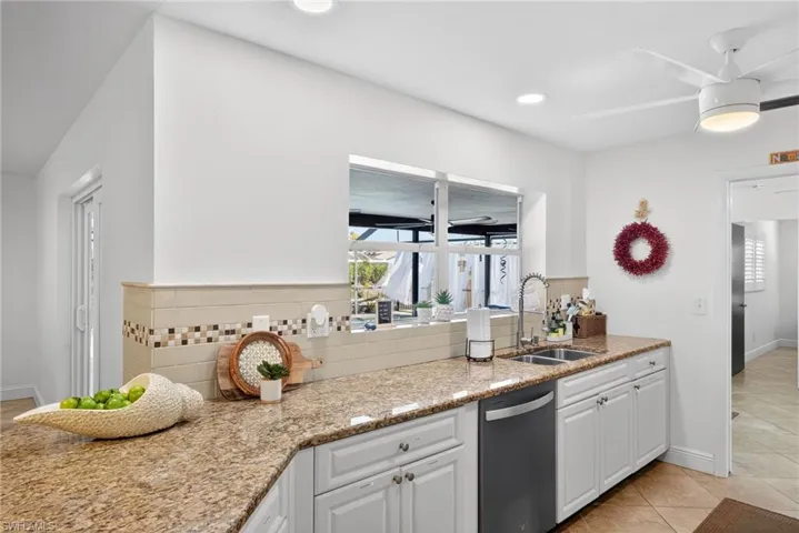 Kitchen featuring light stone counters, white cabinetry, dishwasher, decorative backsplash, and a ceiling fan
