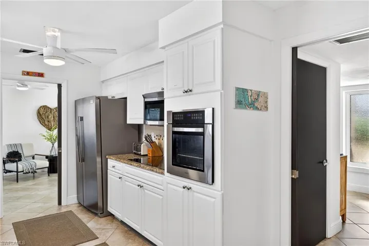 Kitchen featuring stainless steel appliances, ceiling fan, white cabinetry, and dark stone counters