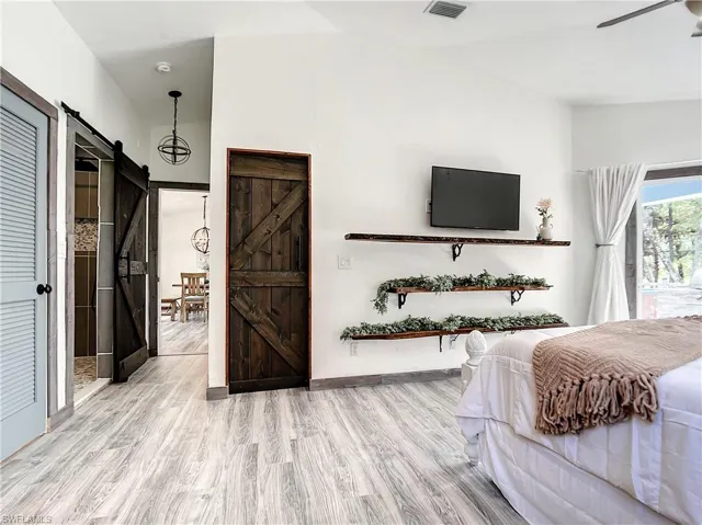 Bedroom with a barn door, light wood finished floors, vaulted ceiling, and a ceiling fan