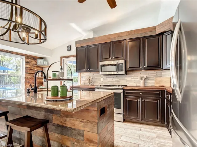 Kitchen featuring stainless steel appliances, vaulted ceiling, dark brown cabinets, an island with sink, and butcher block counters