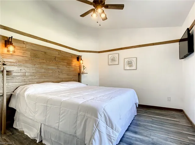 Bedroom with dark wood-type flooring, wood walls, ceiling fan, and lofted ceiling