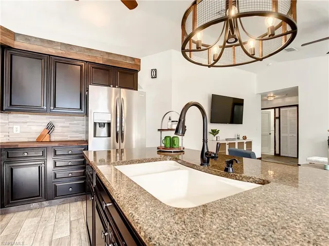 Kitchen featuring a ceiling fan, stainless steel fridge, backsplash, a chandelier, and dark stone countertops