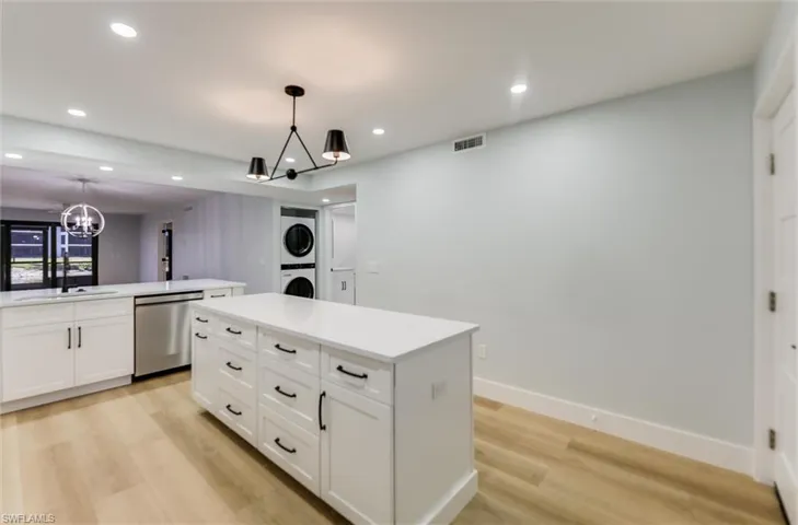 Kitchen with stacked washer / dryer, stainless steel dishwasher, white cabinetry, light wood-type flooring, and a chandelier
