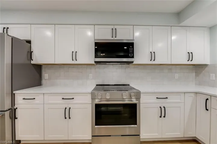 Kitchen with stainless steel appliances, decorative backsplash, light stone counters, and white cabinetry