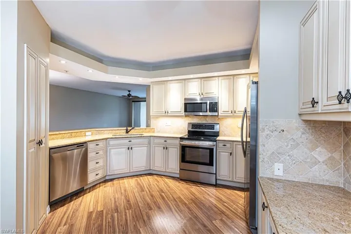 Kitchen featuring appliances with stainless steel finishes, light wood-style floors, a tray ceiling, recessed lighting, and tasteful backsplash