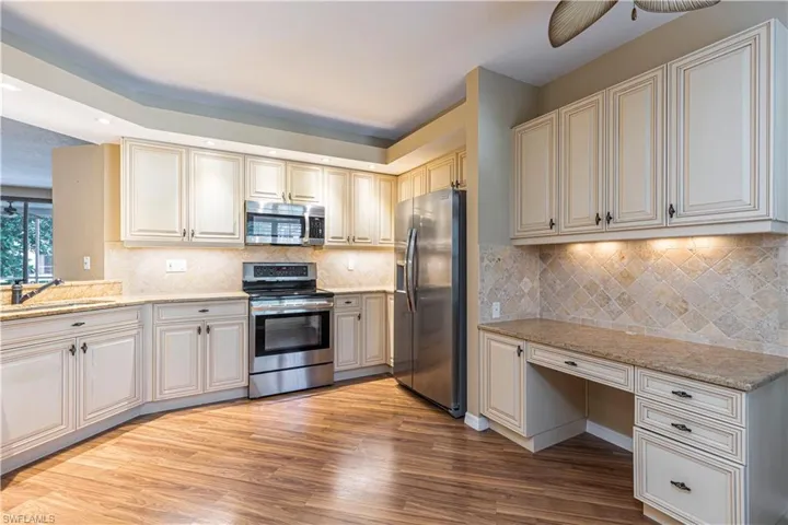 Kitchen featuring appliances with stainless steel finishes, light wood-style flooring, light stone counters, ceiling fan, and tasteful backsplash