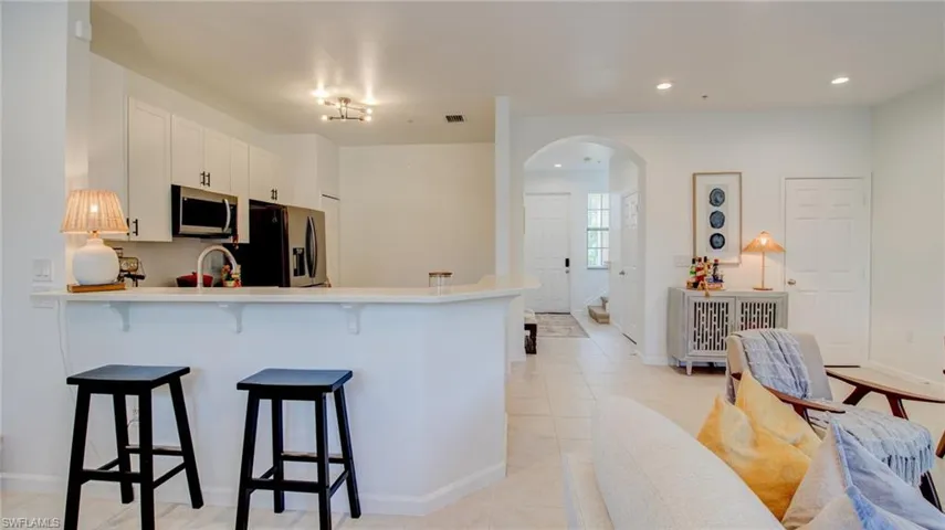 Kitchen featuring a kitchen breakfast bar, a peninsula, light countertops, arched walkways, and white cabinets