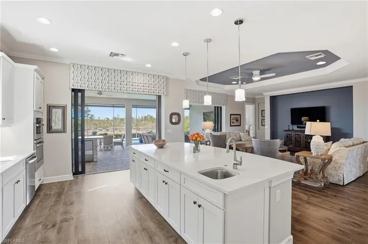 Kitchen with white cabinetry, open floor plan, ceiling fan, ornamental molding, and decorative light fixtures