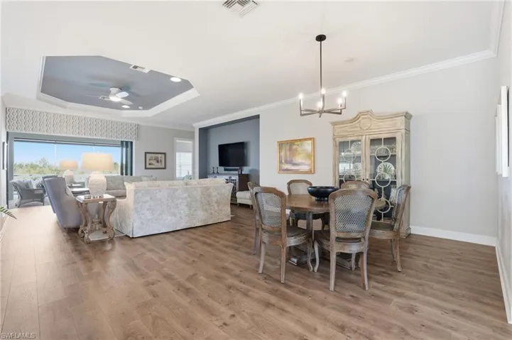 Dining space with crown molding, a tray ceiling, light wood finished floors, a ceiling fan, and a chandelier