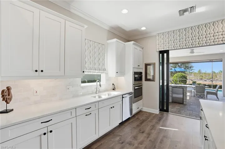 Kitchen with white cabinets, dark wood-type flooring, appliances with stainless steel finishes, healthy amount of natural light, and ornamental molding