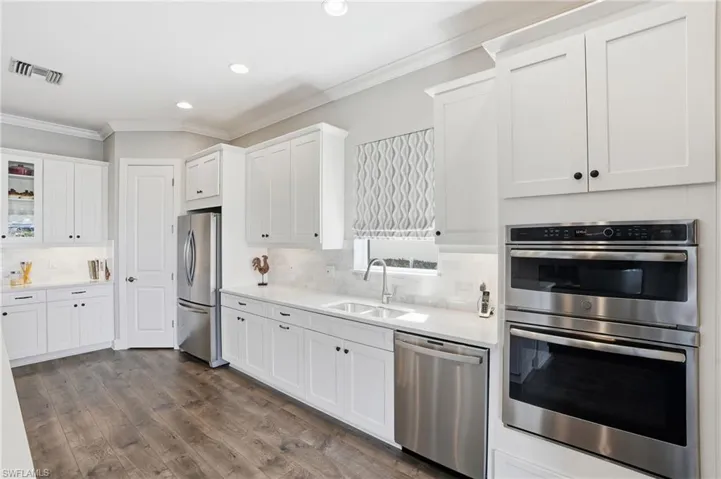 Kitchen with stainless steel appliances, white cabinetry, ornamental molding, dark wood-type flooring, and recessed lighting