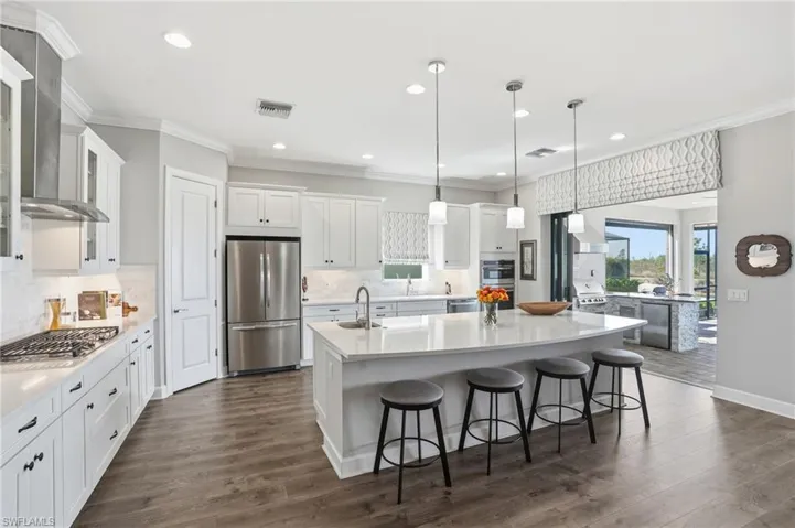 Kitchen featuring white cabinetry, decorative light fixtures, a kitchen bar, appliances with stainless steel finishes, and glass insert cabinets