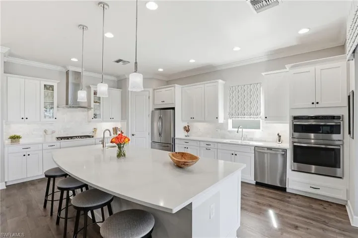 Kitchen featuring ornamental molding, white cabinets, a kitchen breakfast bar, stainless steel appliances, and pendant lighting
