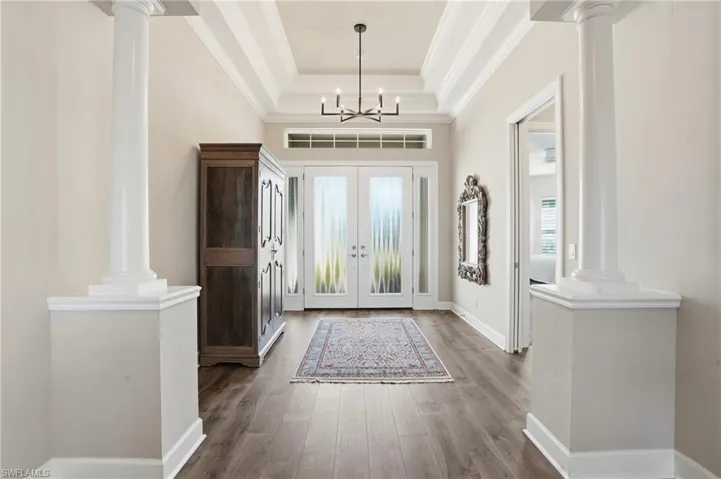 Foyer featuring ornate columns, crown molding, wood finished floors, a raised ceiling, and french doors