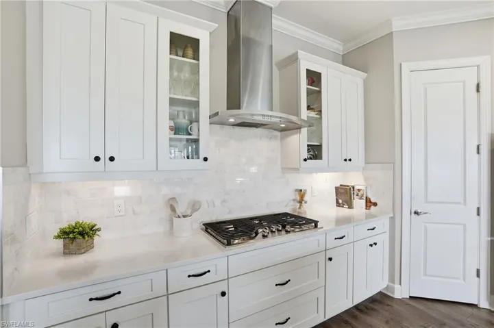 Kitchen featuring white cabinets, wall chimney range hood, ornamental molding, light stone countertops, and stainless steel gas cooktop